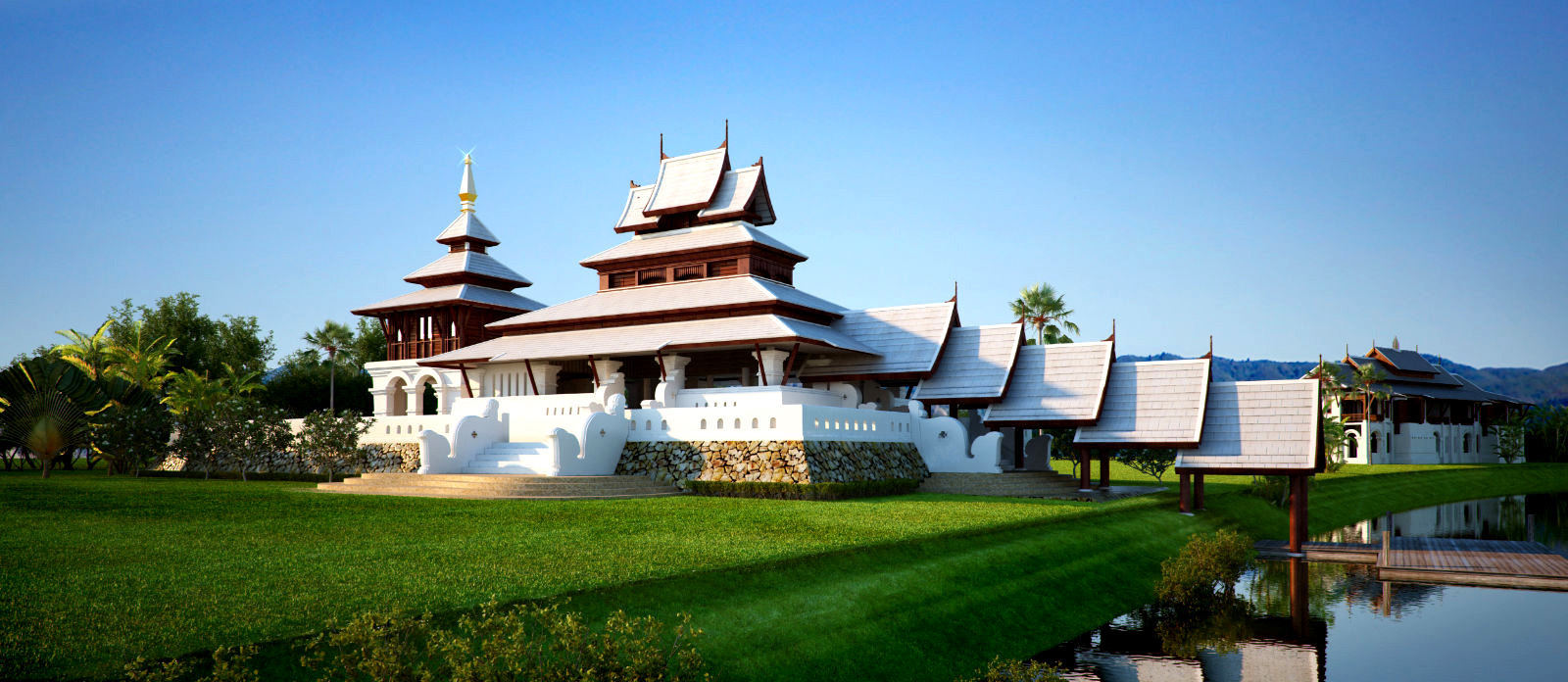Traditional Asian-style white and wood building with tiered roofs on a green lawn beside a pond under a clear blue sky